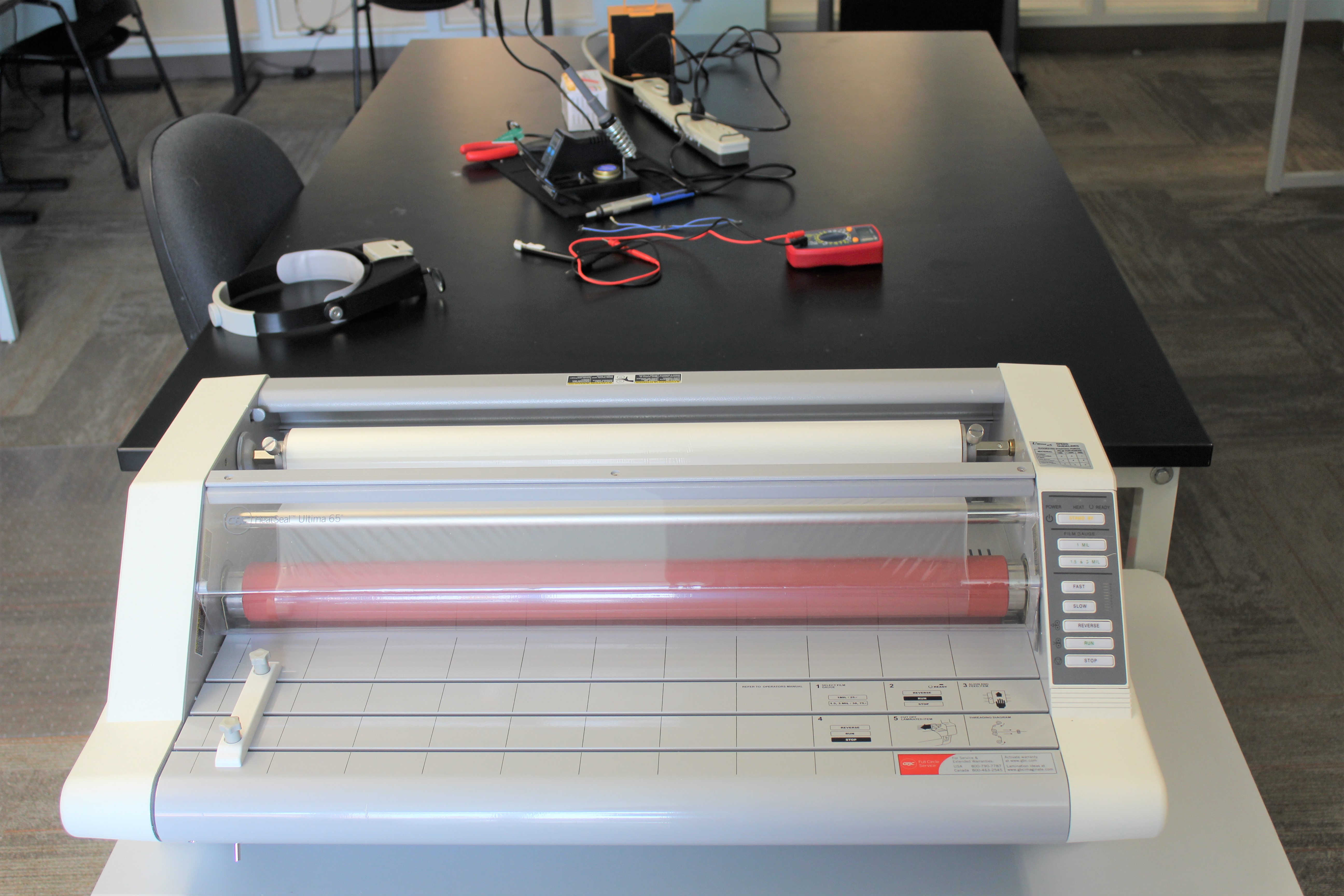 Laminator next to a work table with soldering equipment on it.