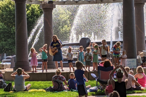 Photo of singer and children on stage in front of a fountain.