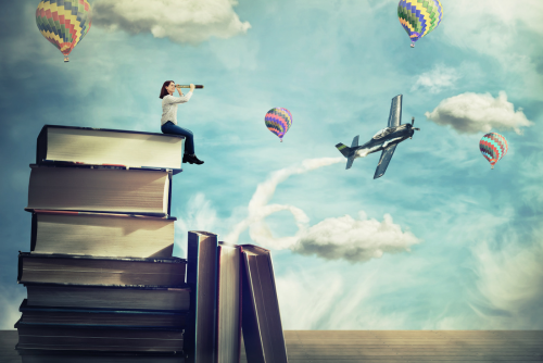 A person sitting on top of a pile of books with a telescope surrounded by airplanes and hot air balloons.