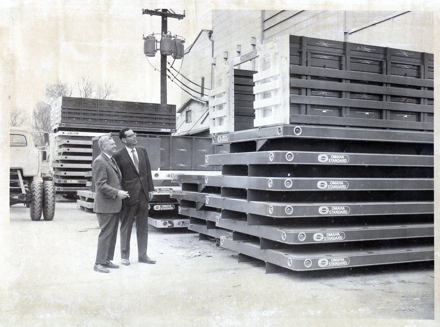 A photo of two men looking at a stack of Omaha Standard trailer beds