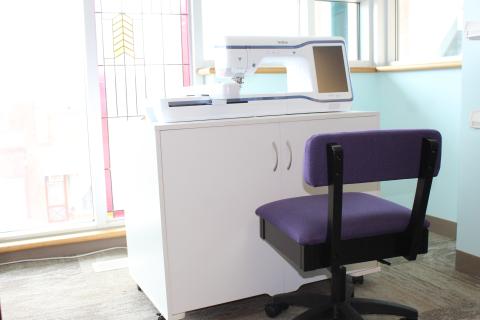 Embroidery machine on a table with purple swivel chair in front