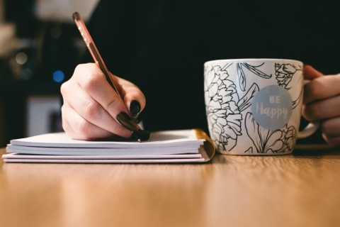 a person writing in a notebook and holding a mug