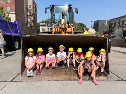 Children sitting in the bucket of a tractor.