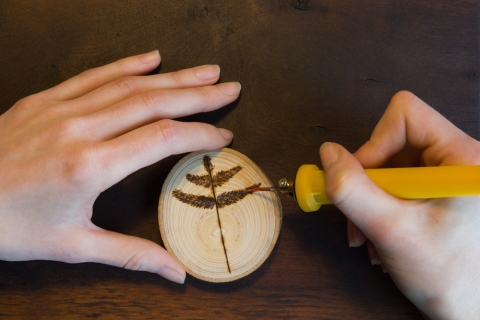 person burning a tree leaf onto wood with a wood burning tool