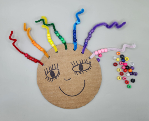 Cardboard face with pipe cleaner and beaded hair.