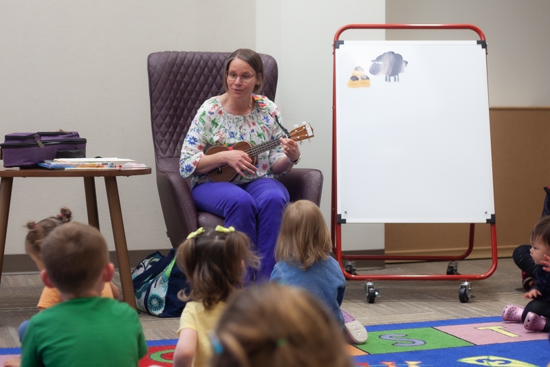 Person playing a ukulele and singing to children.