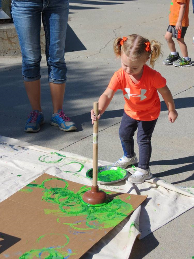Child painting on cardboard with a plunger