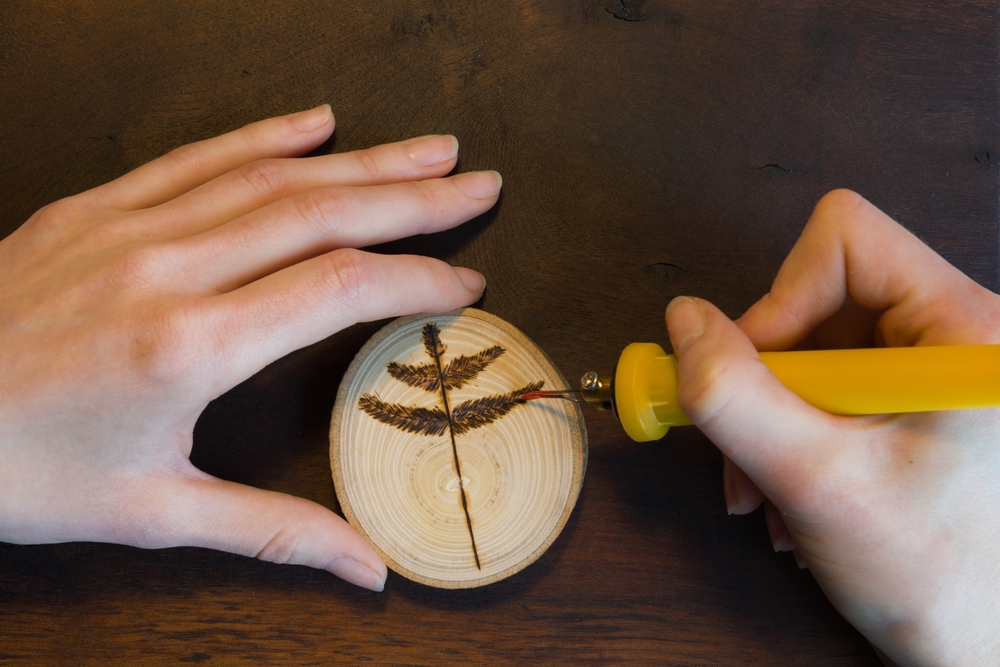 person burning a tree leaf onto wood with a wood burning tool
