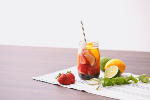 fruit drink in jar with strawberries, limes, lemons, and mint on cloth 